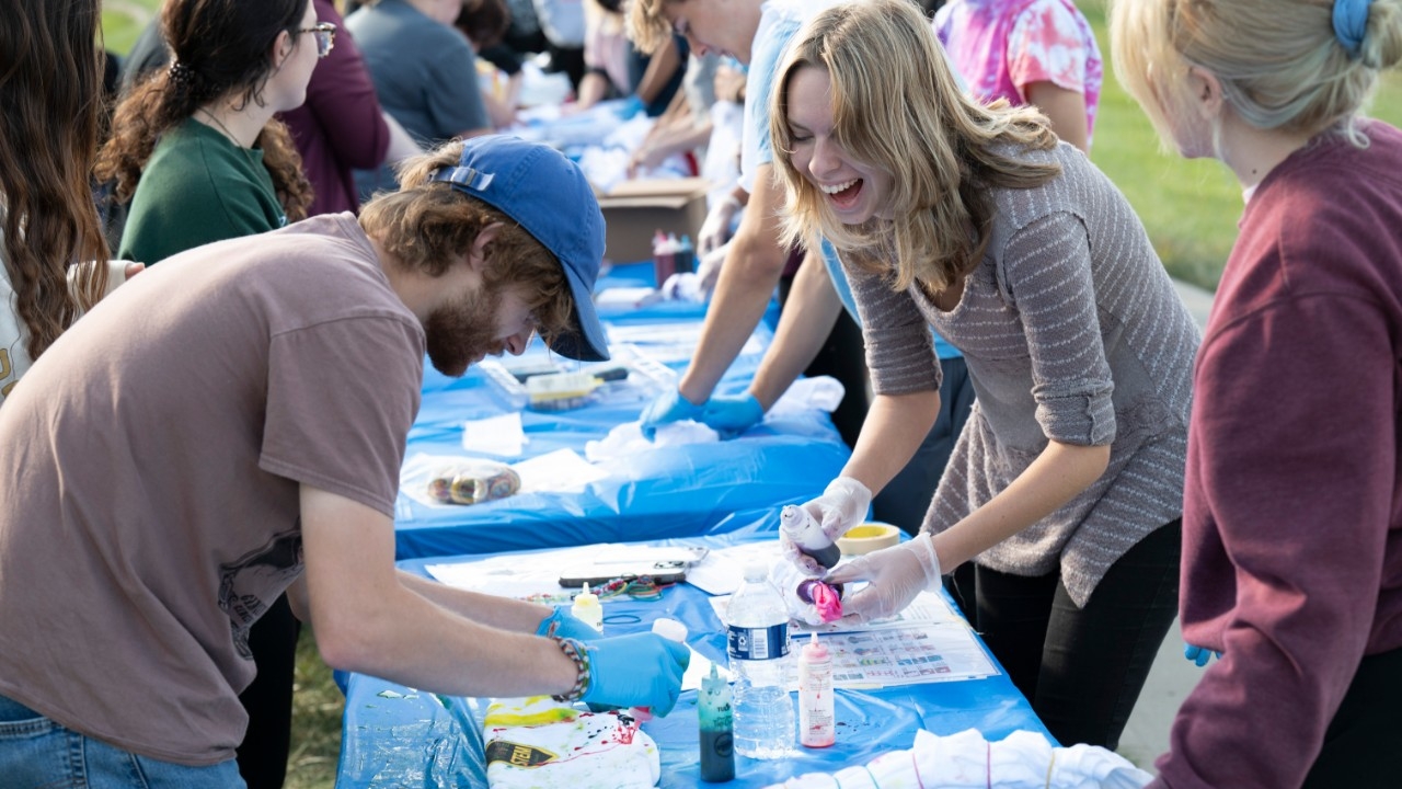 NKU STEM majors smiling and laughing while making custom tie-dye shirts outside on a sunny day.