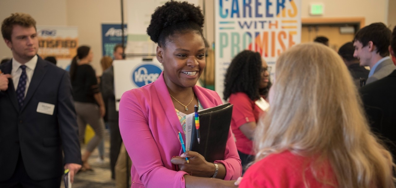 Student wearing professional attire shaking hands with a prospective employer at a career fair.