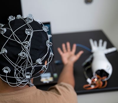 Rear view of someone wearing sensors on their head connected to a robot arm.